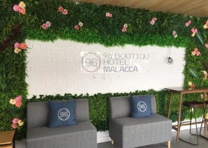 A hotel lobby with a white brick wall, a green leafy wall, and two grey sofas with pillows. - 96 Boutique Hotel (Melaka)