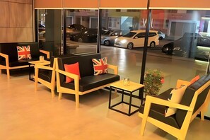 Een moderne hotellobby met zitgedeeltes, een tafeltje en een uitzicht op geparkeerde auto's door grote ramen.