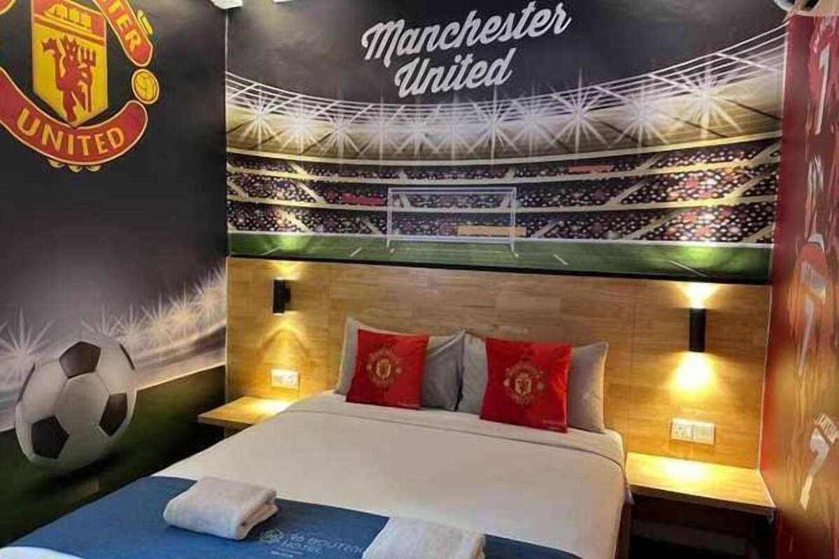 Habitación de hotel con cama, almohadas, un mural en la pared con un estadio y el logotipo del Manchester United.