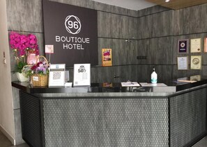 A hotel reception desk with a sign for '96 Boutique Hotel', a QR code, a promotional sign offering a 50% discount, and a framed certificate on the wall. - 96 Boutique Hotel (Melaka)