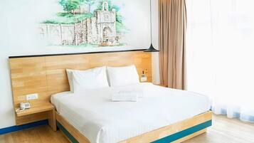 A hotel room with a bed, a bedside table with a phone, a wall-mounted lamp, and a painting of a building.