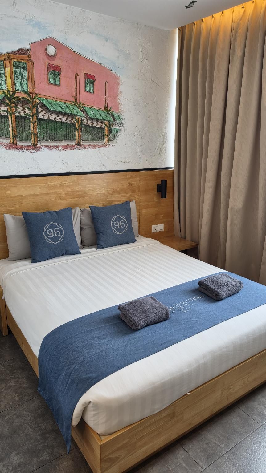A hotel room with a bed, pillows, a headboard, a wall mural, and a window with curtains.