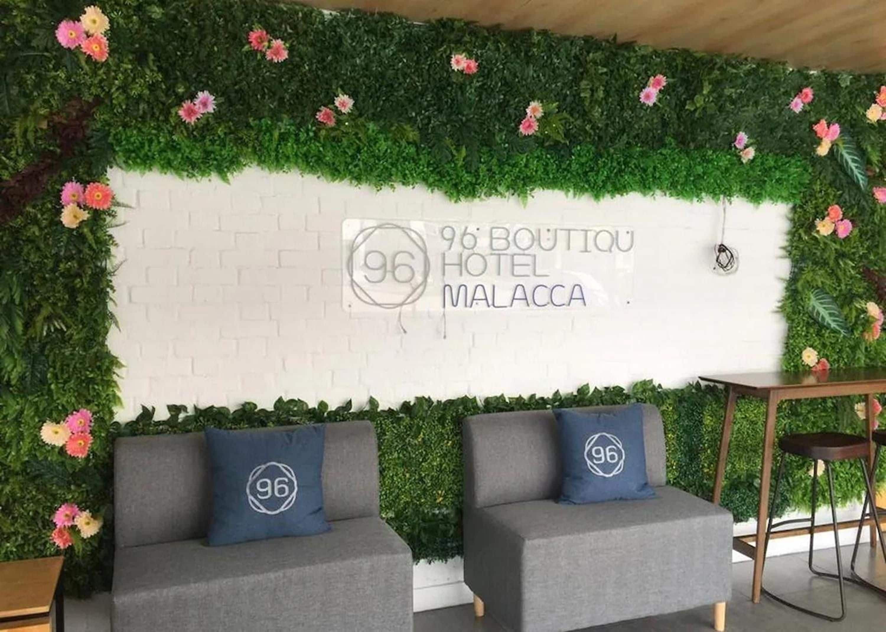 A hotel reception area with a white brick wall, a green vertical garden, and two grey sofas with pillows.