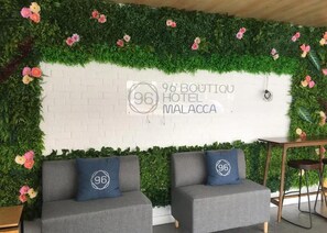 Zona de recepción de hotel con pared de ladrillo blanco, jardín vertical verde y dos sofás grises con almohadones.