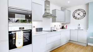 A modern kitchen with white cabinetry, a Bosch oven, a built-in stove, a large clock, and a wooden floor.