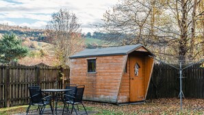 Un cobertizo de madera con techo inclinado, una ventana pequeña y una puerta con un cascabel.