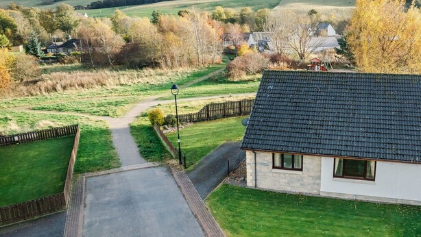 Casa rural con camino de entrada pavimentado que lleva a una reja, rodeada de césped cuidado y un sendero.