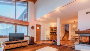 A spacious living room with a wooden floor, a television on a wooden stand, a fireplace, and a staircase leading to another level. - Cosy apartment in villa for 5 people with WIFI, TV, terrace and panoramic view (Bleggio Superiore)