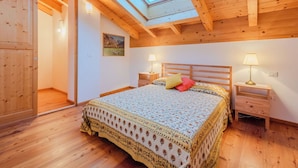 A bedroom with a skylight, wooden beams, a bed with patterned bedding, bedside lamps, and a painting on the wall. - Cosy apartment in villa for 5 people with WIFI, TV, terrace and panoramic view (Bleggio Superiore)