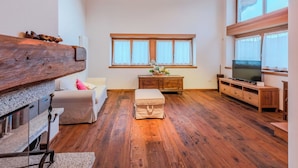 A spacious living room with wooden floors, a large window with curtains, a television, and a wooden bench. - Cosy apartment in villa for 5 people with WIFI, TV, terrace and panoramic view (Bleggio Superiore)