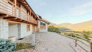 A stone-paved courtyard with a wooden fence, a stone wall, and a view of mountains in the background. - Cosy apartment in villa for 5 people with WIFI, TV, terrace and panoramic view (Bleggio Superiore)