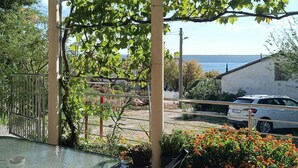 Ein Balkon mit Glastisch, Blumentöpfen und Blick auf ein weißes Auto und ein Gebäude im Hintergrund.
