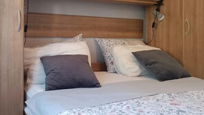 Ein kleines Bett mit Holz Kopfteil, zwei Kissen und einer zudeckenden Bettwäsche mit Blumenmuster.