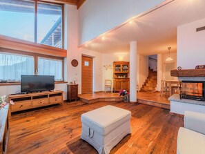 A spacious living room with a wooden floor, a television on a wooden stand, a fireplace, and a staircase leading to another level.