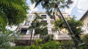 A multi-story building with balconies, surrounded by lush greenery and palm trees. - Express by M Village Hoang Van Thu, a brand of Modern Village Lifestyle (Ho Chi Minh City)
