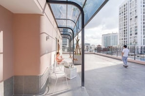 Een modern buiten zitgedeelte met glazen balustrade, een persoon zittend en een andere persoon staand.