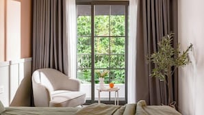 A room with a bed, a chair, a small table with a vase and an orange, and a window with curtains. - Express by M Village Hoang Van Thu, a brand of Modern Village Lifestyle (Ho Chi Minh City)