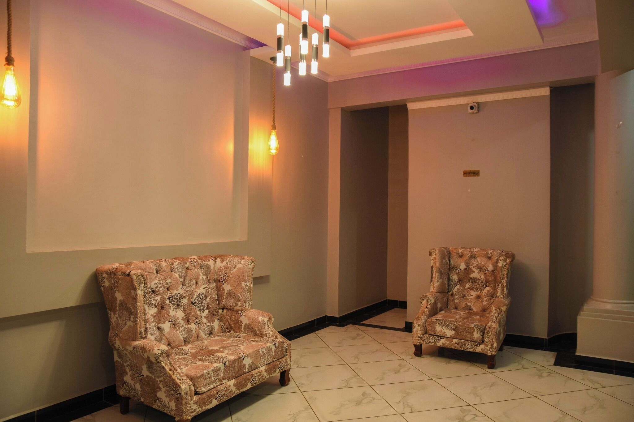 A hallway with two patterned armchairs, a modern chandelier, and a tiled floor.