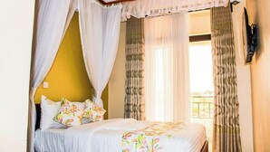 A bedroom with a bed, white curtains, and a view of the outside. - Golden Palace Hotel Eldoret (Eldoret)