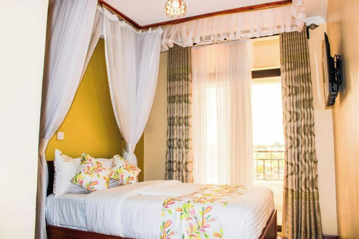 A bedroom with a bed, white curtains, and a view of the outside.