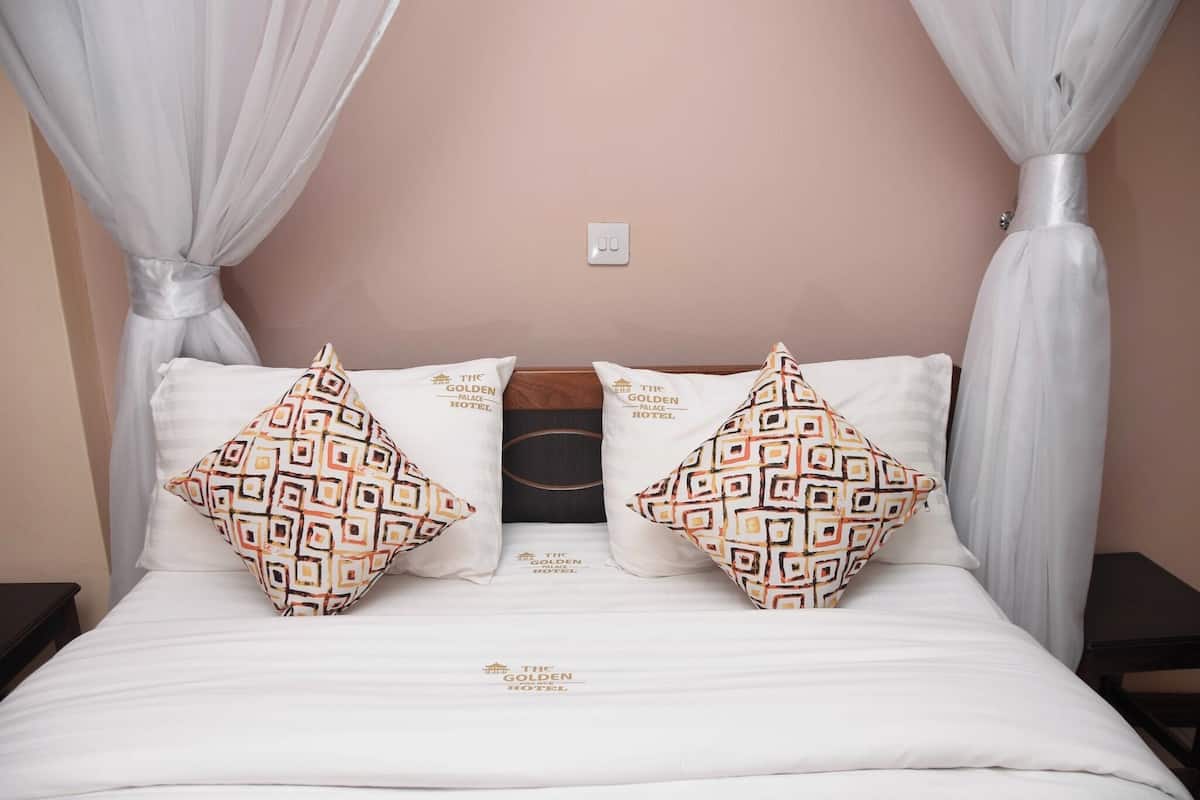 A bed with white bedding and patterned pillows, a wooden headboard, and sheer curtains.