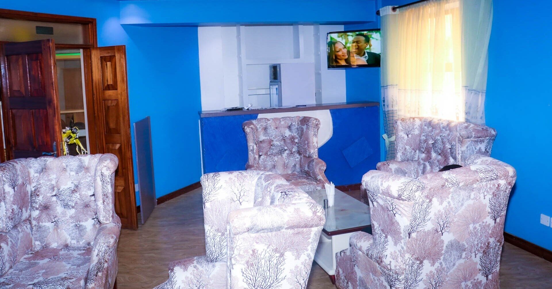 A room with blue walls, a wooden door, and a television mounted on the wall.