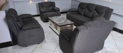 A modern living room with a sectional sofa, two recliner chairs, and a marble-tiled floor.