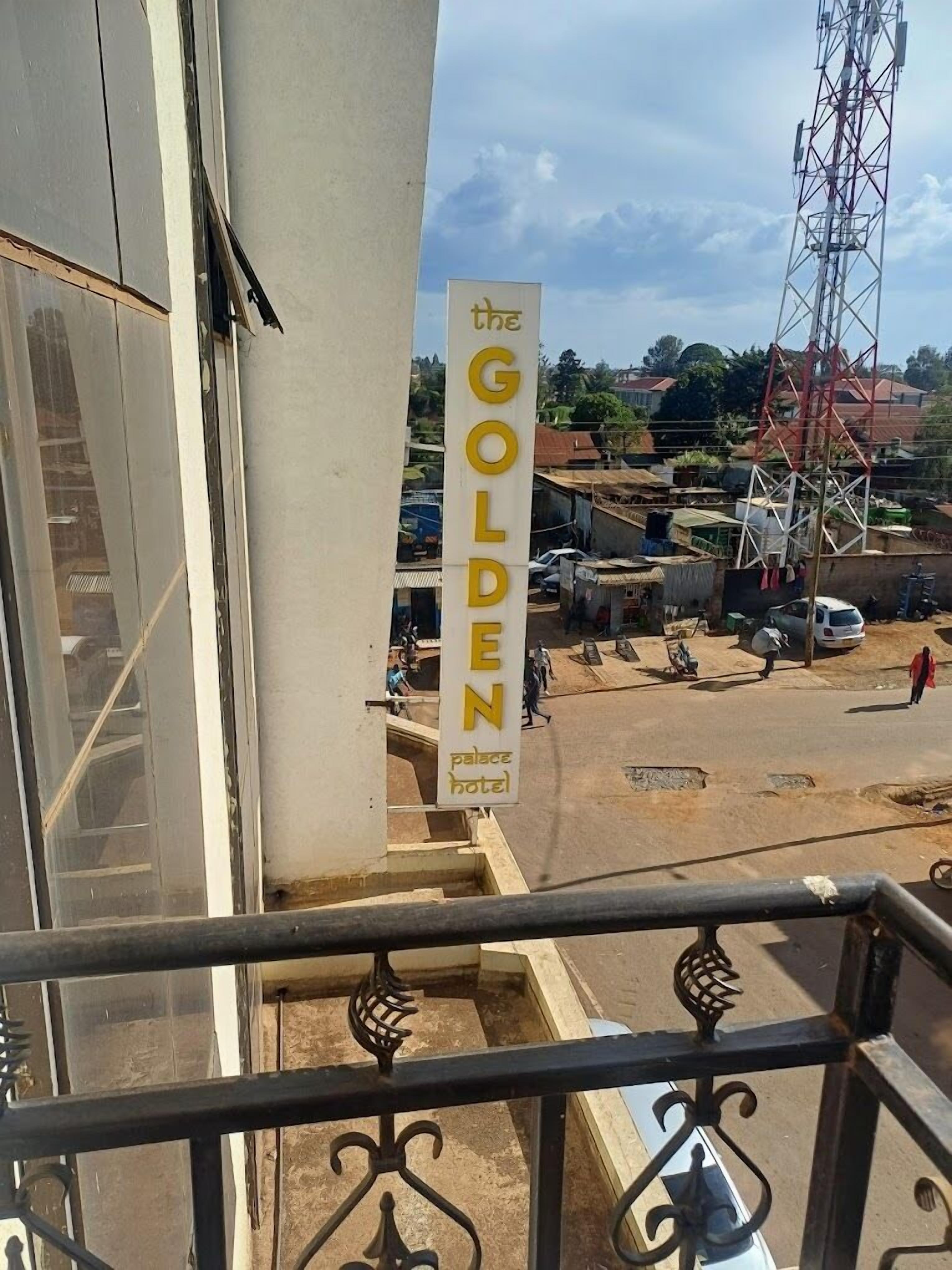 Een hotelschild met de naam "The Golden Palace Hotel" en een uitzicht op een straat met gebouwen en een elektriciteitspylon.