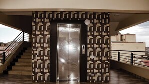 A modern elevator with a geometric patterned wall, a staircase on the left, and a balcony on the right. - Golden Palace Hotel Eldoret (Eldoret)