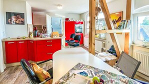 Una cocina moderna con armarios rojos, estructura de vigas de madera y una zona de comedor con una mesa dispuesta para dos personas.