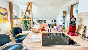 Una cocina moderna con estufa integrada, una silla de madera, una cafetera roja y una estantería.