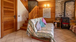 A cozy room with a wooden staircase, a bed with patterned bedding, a map on the wall, and a wood-burning stove. - Beautiful private villa for 7 guests with WIFI, TV and pets allowed (Casone)
