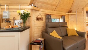 Interior acogedor de una cabaña con kitchenette, un sofá de cuero marrón con cojines amarillos y una mesita de madera.