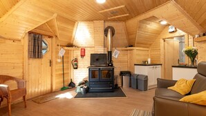 Acogedor interior de cabaña de madera con chimenea, un sofá y una zona de comedor.