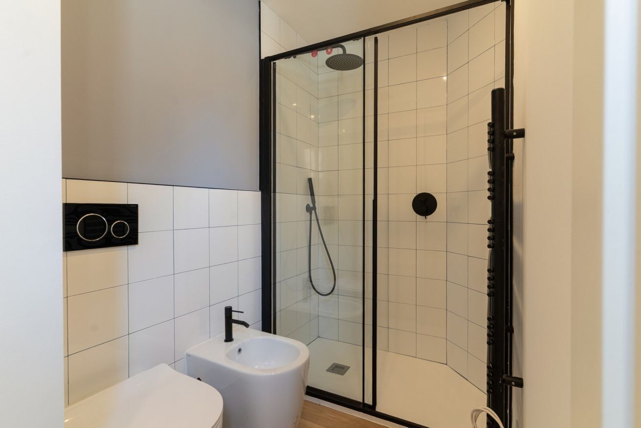 Ein modernes Badezimmer mit einer gläsernen Dusche, einem weißen Waschbecken und einem schwarzen Handtuchhalter.