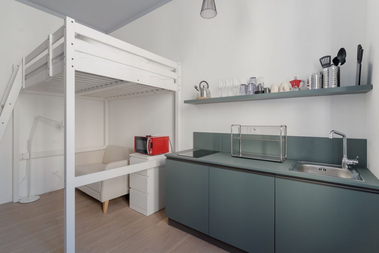 A compact kitchen with a built-in microwave, a sink, and a shelf with kitchen utensils.