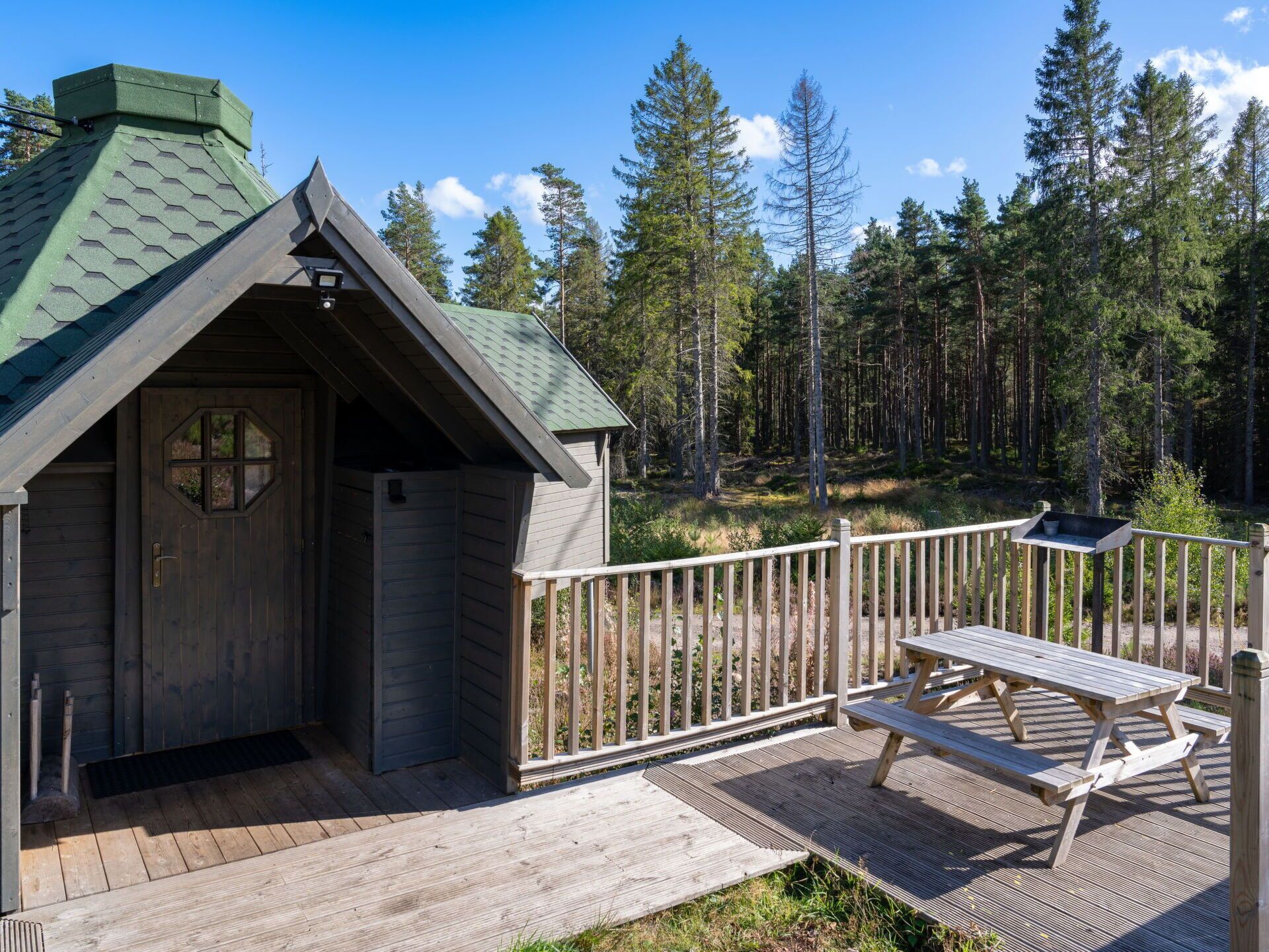 Eine Holzhütte mit einer sechseckigen Tür, einem Picknicktisch und einer Holzterrasse.