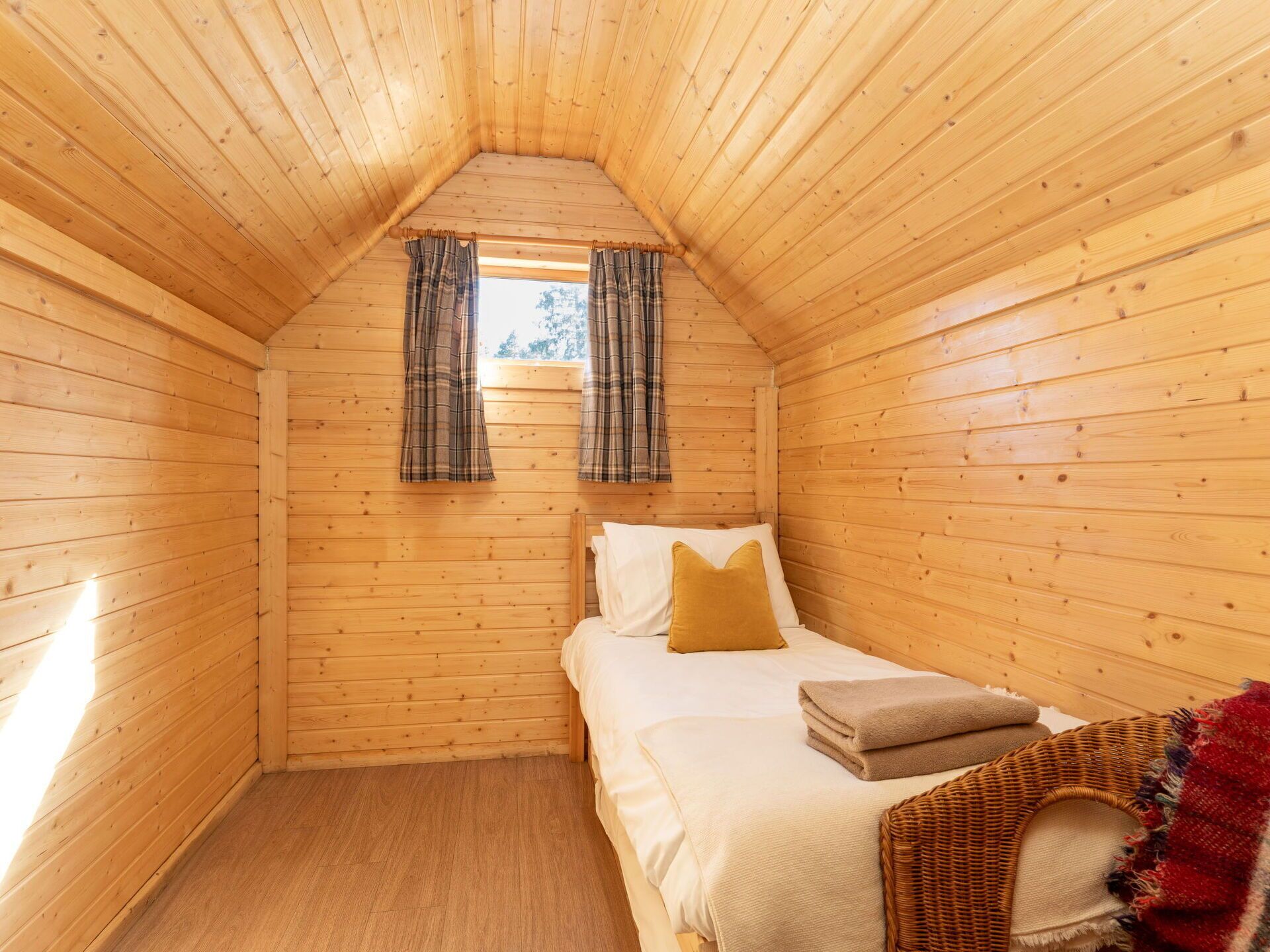 Um quarto de cabana de madeira aconchegante, com cama, cortinas xadrez e uma janela.