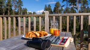 A wooden deck with a picnic setup including croissants, a jug of orange juice, and a book.