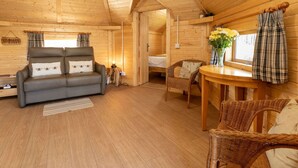 A cozy cabin interior with a sofa, wicker chairs, a small table, and a window with curtains.