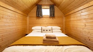 A cozy, wooden-paneled room with a bed, a window with curtains, and a small window above the bed.