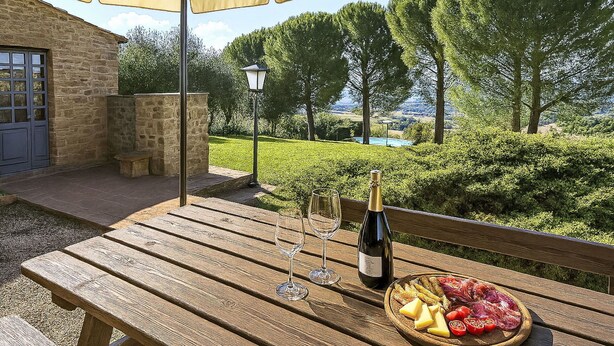 Un tavolo di legno con una bottiglia di vino, bicchieri e un piatto di cibo sotto un ombrellone.