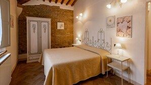 A bedroom with a bed, bedside tables, a wardrobe, and a brick wall.