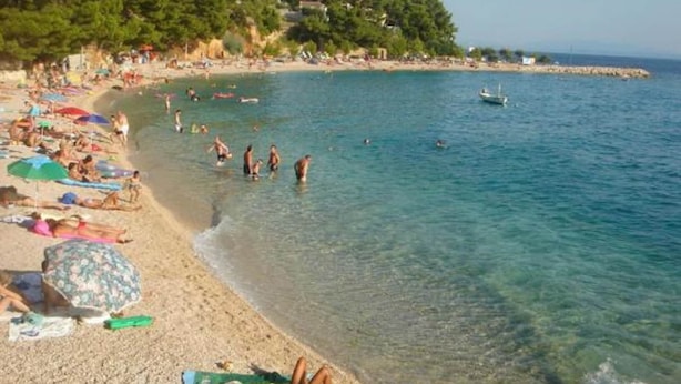 Une plage où des gens se prélassent au soleil et se baignent, avec une eau claire et un bateau visible au loin.