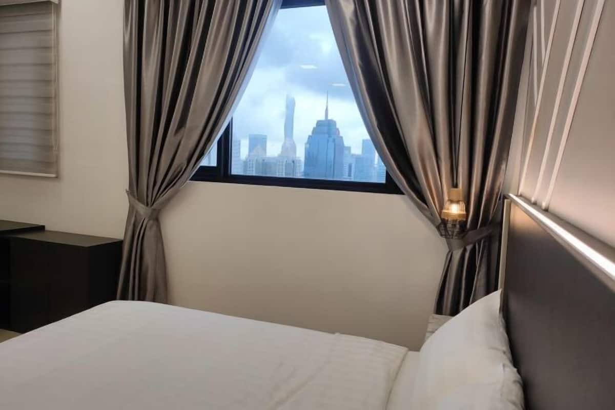 Habitación de hotel con cama, cortinas, mesita de noche y vistas a un horizonte urbano a través de la ventana.