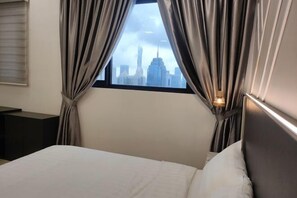 A hotel room with a bed, curtains, a nightstand, and a view of a city skyline through a window. - The Luxury Stay KL (Kuala Lumpur)