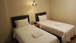 Une chambre d’hôtel avec deux lits simples, chacun recouvert d’une courtepointe et doté d’un oreiller, une table de chevet avec une lampe, et une petite table de nuit avec un téléphone et quelques objets.
