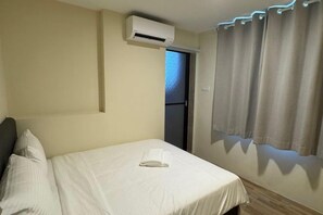 Una habitación de hotel con una cama, un equipo de aire acondicionado, una puerta y cortinas.