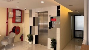 Un ascenseur moderne doté d’un écran numérique, d’un extincteur et d’un tuyau d’incendie rouge fixé au mur.