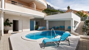 A modern building with a swimming pool, sun loungers, and a staircase leading to a balcony.